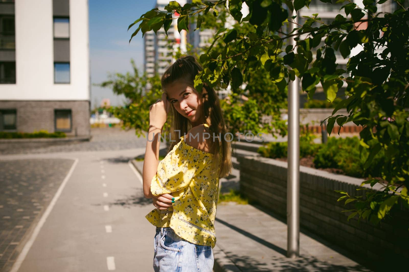 Young beautiful woman is strolling outdoors in the yard, against the backdrop of greenery and houses, warm summer sunny day