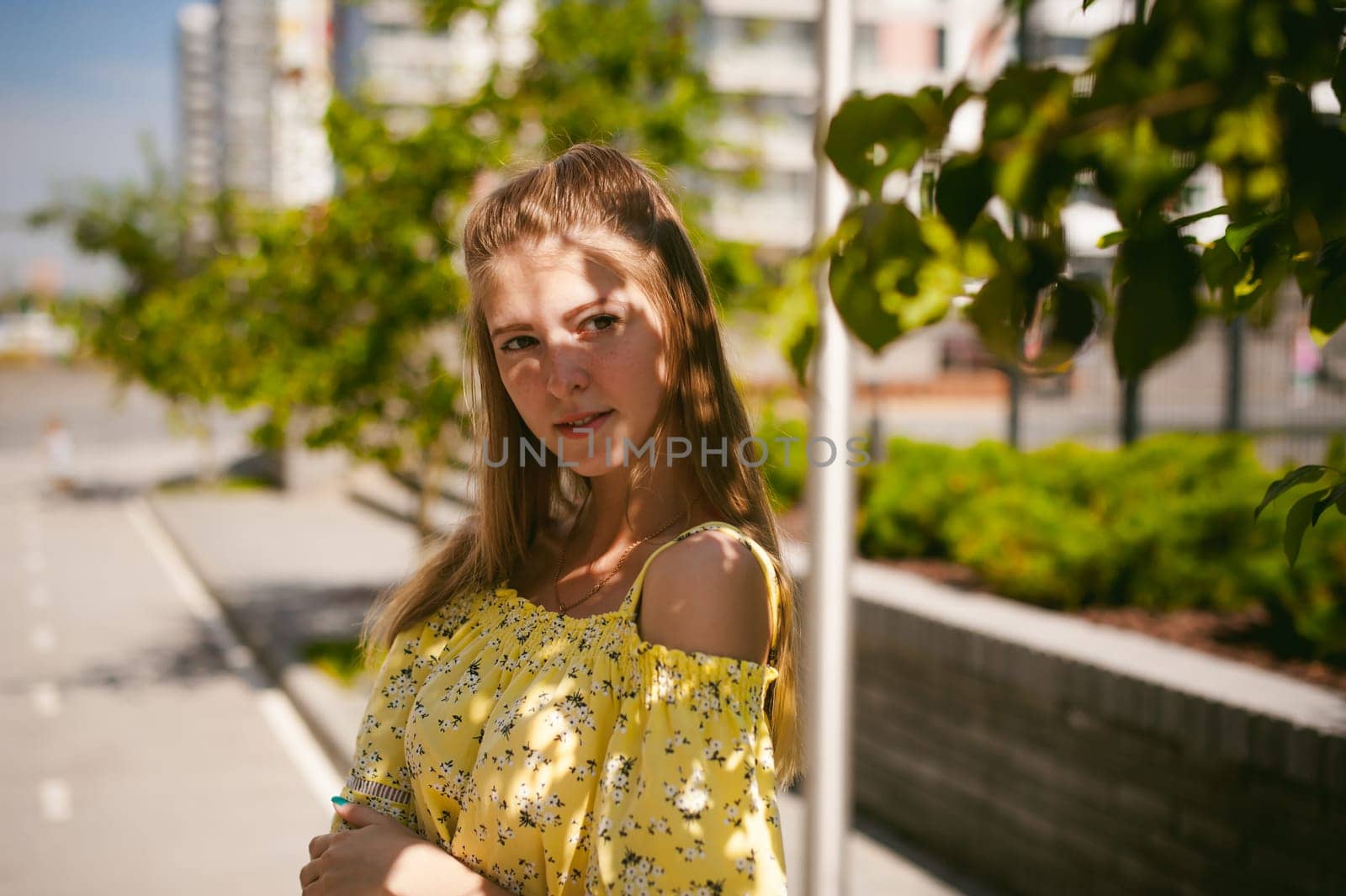 Young beautiful woman is strolling outdoors in the yard, against the backdrop of greenery and houses, warm summer sunny day