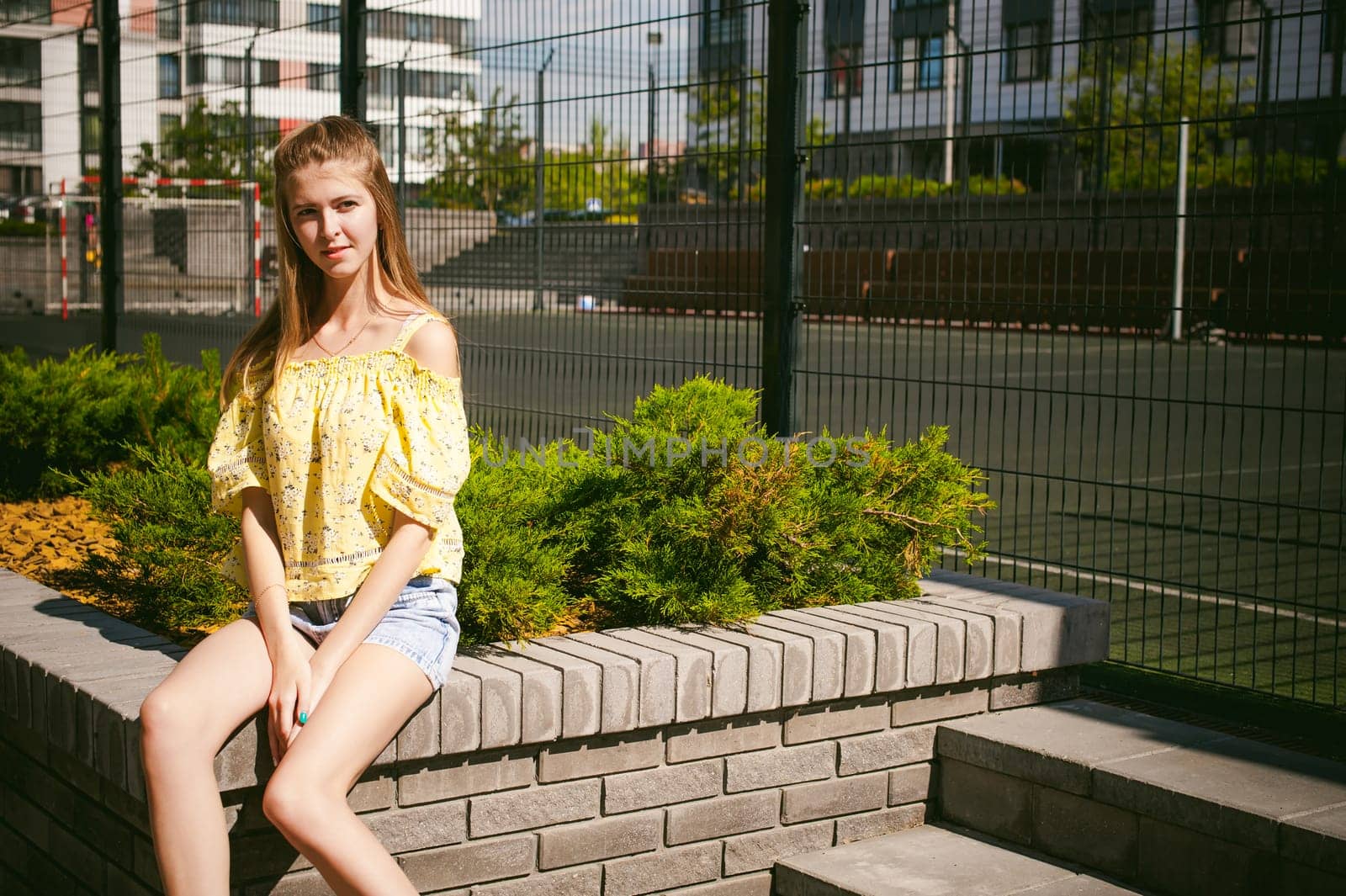 Young beautiful woman is strolling outdoors in the yard, against the backdrop of greenery and houses, warm summer sunny day