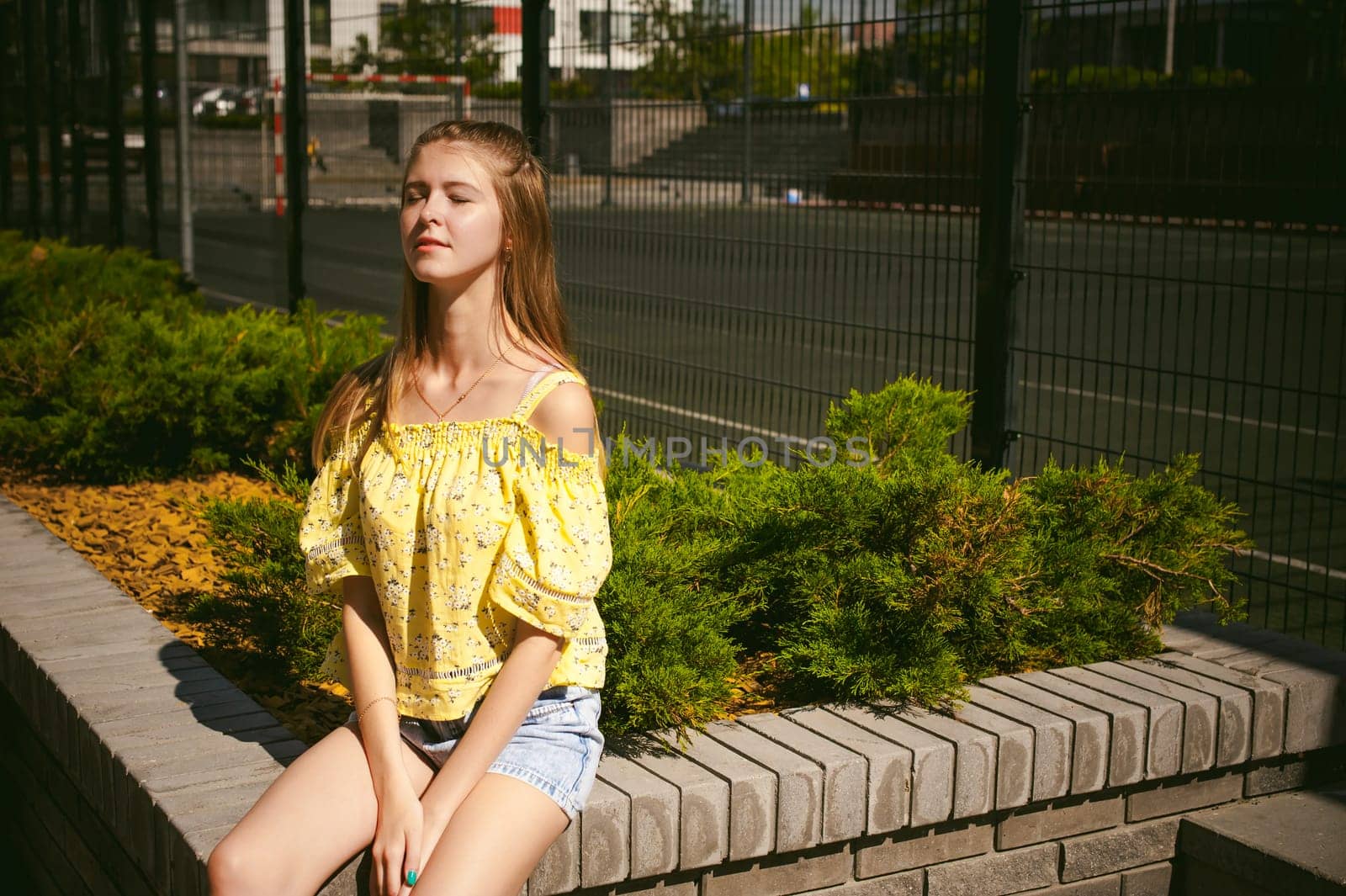 Young beautiful woman is strolling outdoors in the yard, against the backdrop of greenery and houses, warm summer sunny day