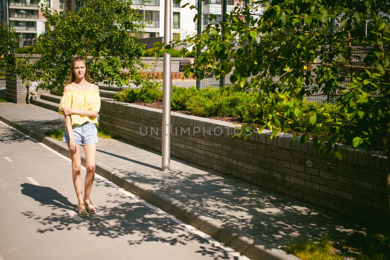 Young beautiful woman is strolling outdoors in the yard, against the backdrop of greenery and houses, warm summer sunny day