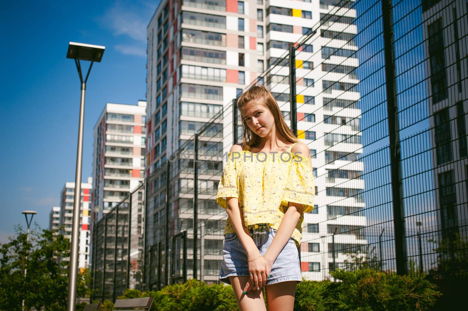 Young beautiful woman is strolling outdoors in the yard, against the backdrop of greenery and houses, warm summer sunny day