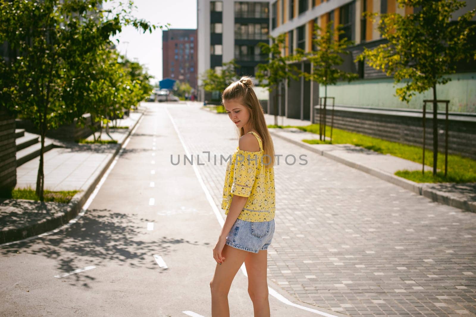 Young beautiful woman is strolling outdoors in the yard, against the backdrop of greenery and houses, warm summer sunny day