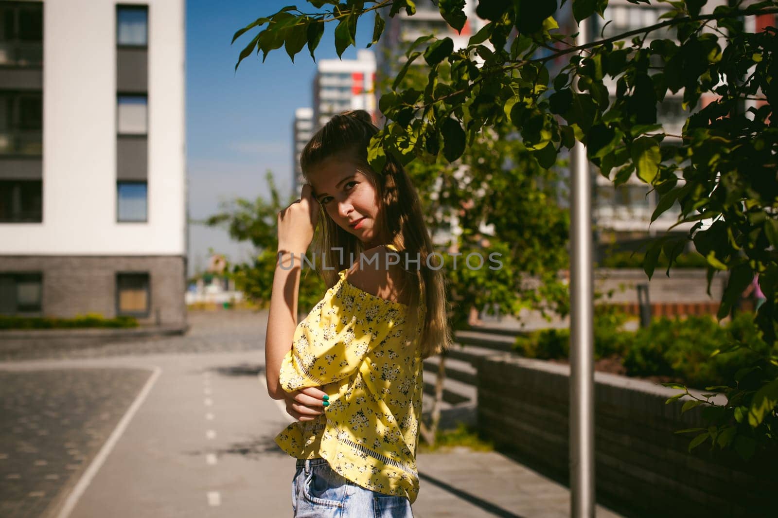 Young beautiful woman is strolling outdoors in the yard, against the backdrop of greenery and houses, warm summer sunny day