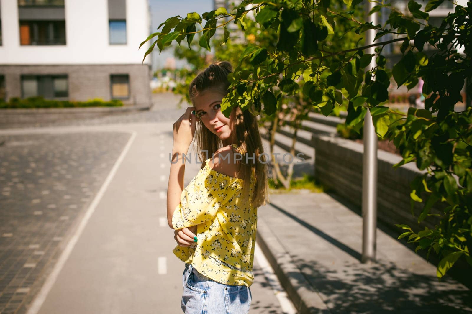 Young beautiful woman is strolling outdoors in the yard, against the backdrop of greenery and houses, warm summer sunny day