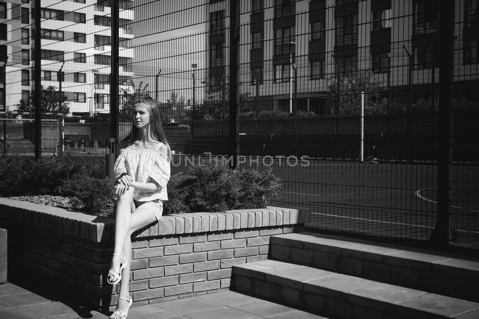 Young beautiful woman is strolling outdoors in the yard, against the backdrop of greenery and houses, warm summer sunny day