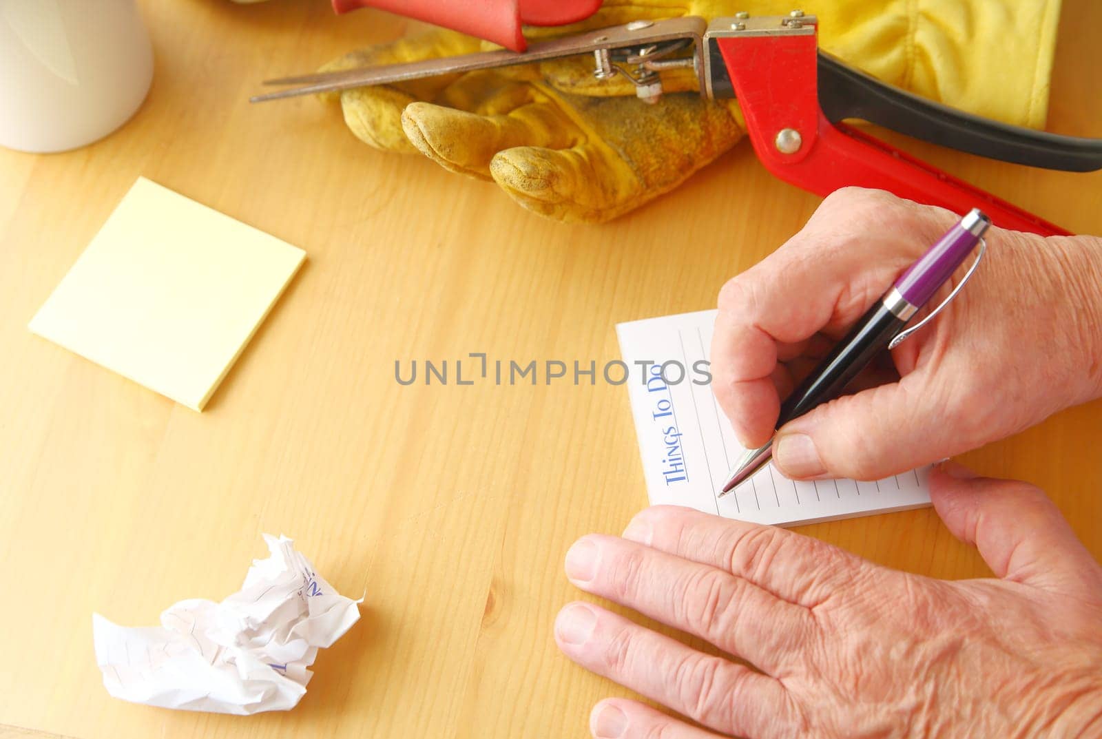 Overhead of man writing a to do list with crumpled paper, notepad, coffee cup, gardening glove and grass cutters