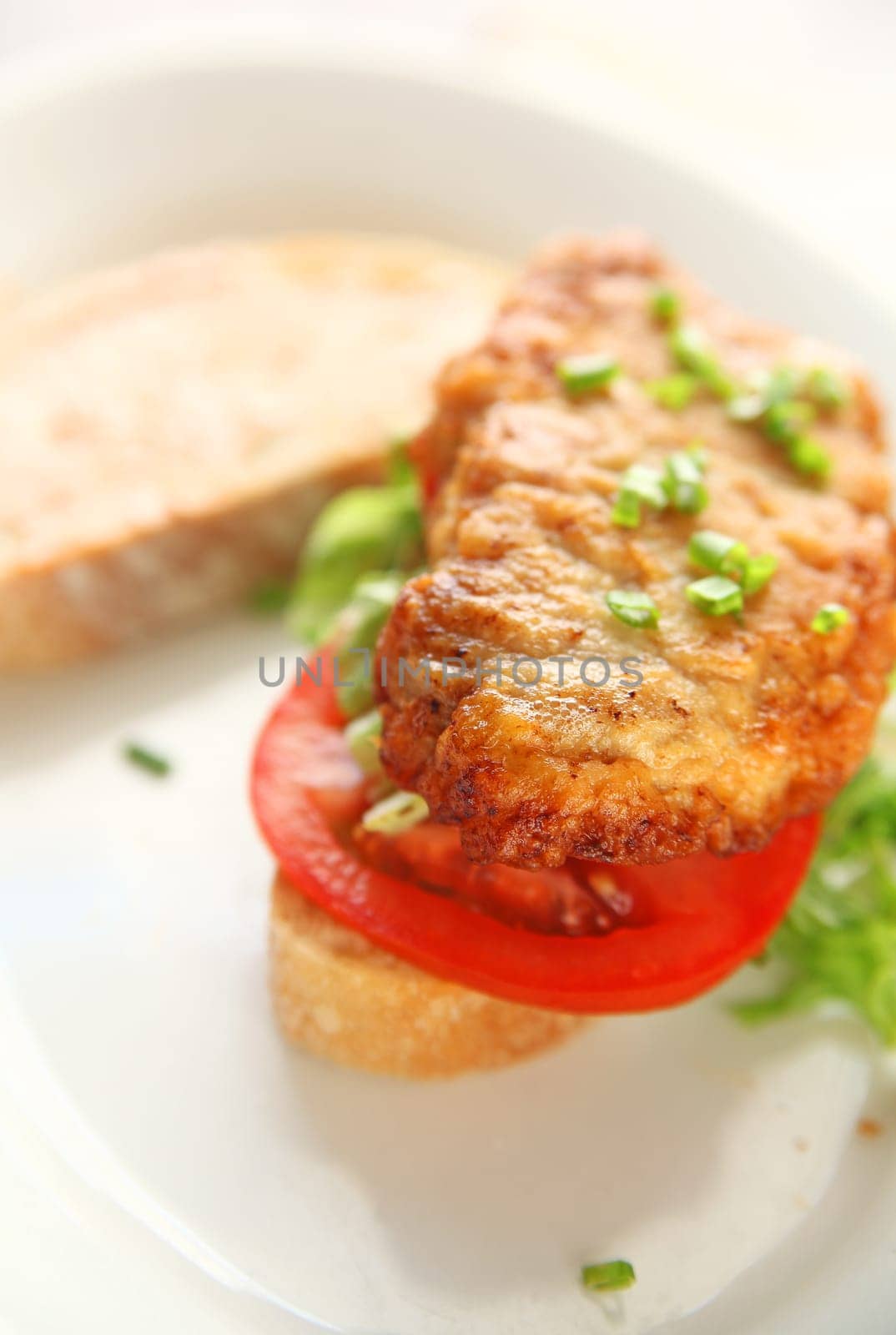 A battered and fried pork cutlet with tomato, chopped lettuce and scallions on artisan bread