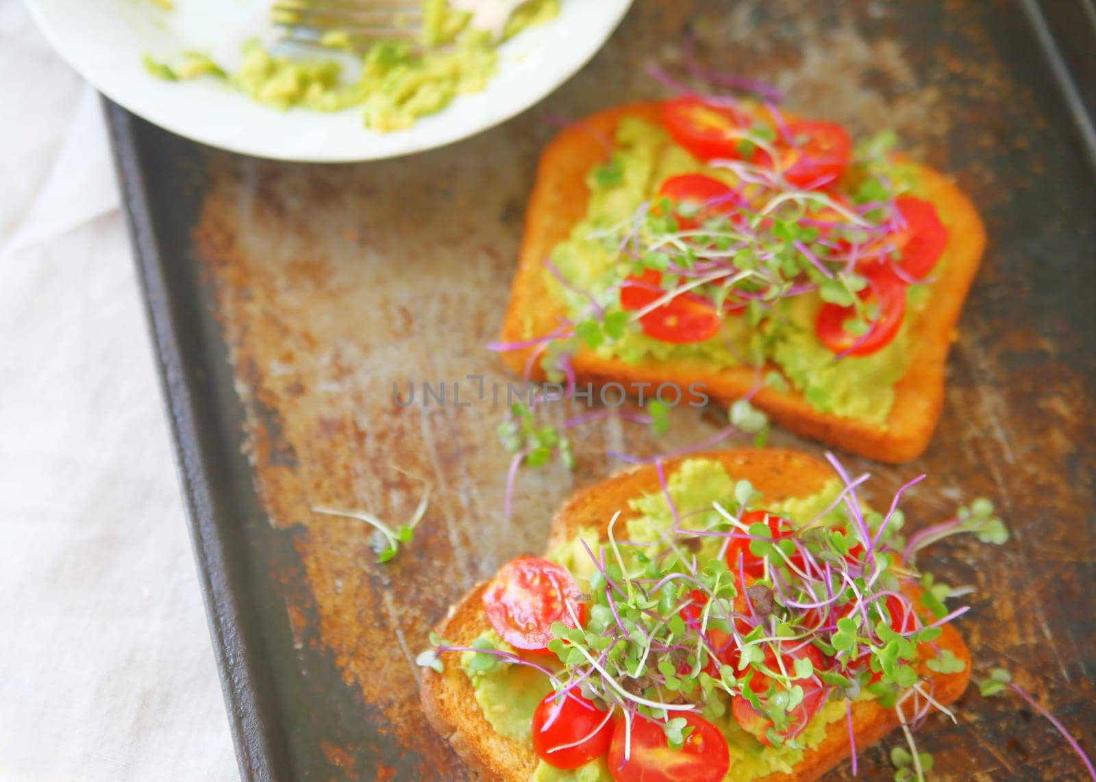Overhead view of avocado toast with cherry tomatoes and sprouts on an old baking tray with room for text