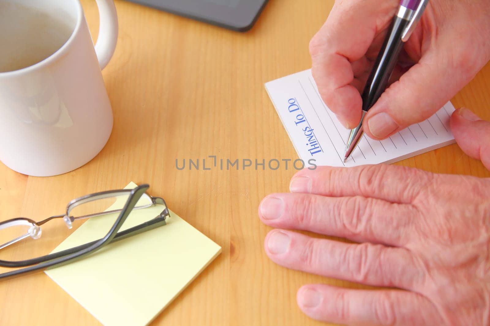 A man with a pen, glasses, note pads and coffee cup on a desk