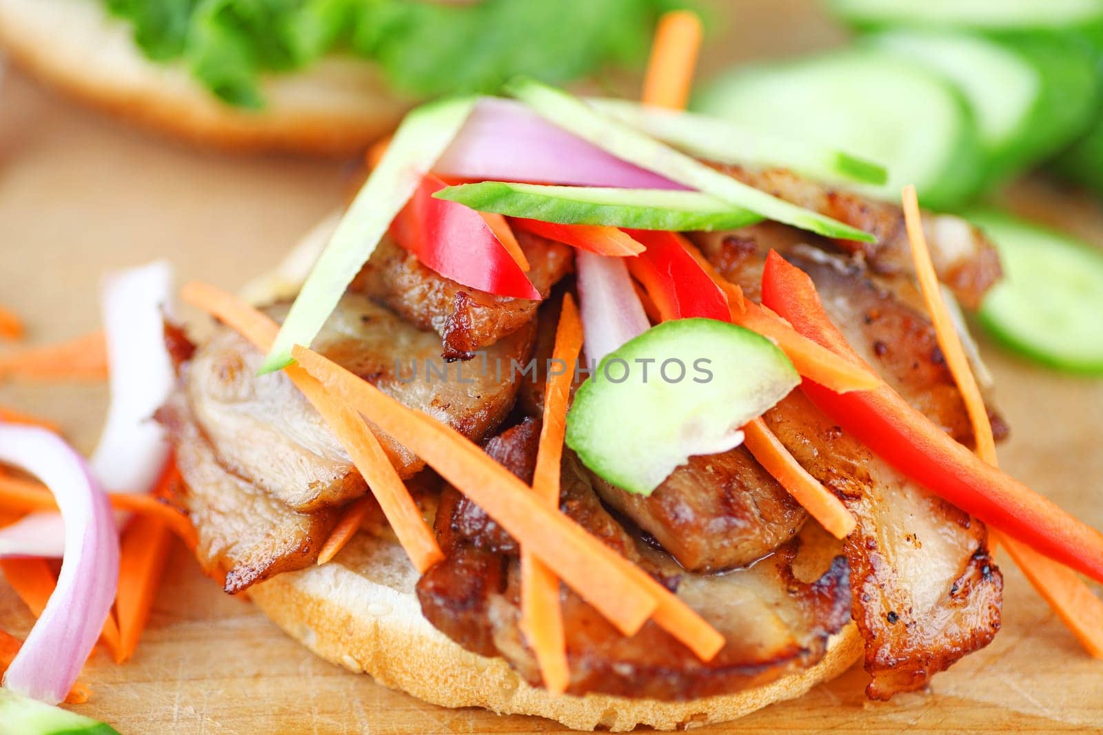 roast pork slices with raw cucumber, bell pepper, onion and carrot on sesame seed bun