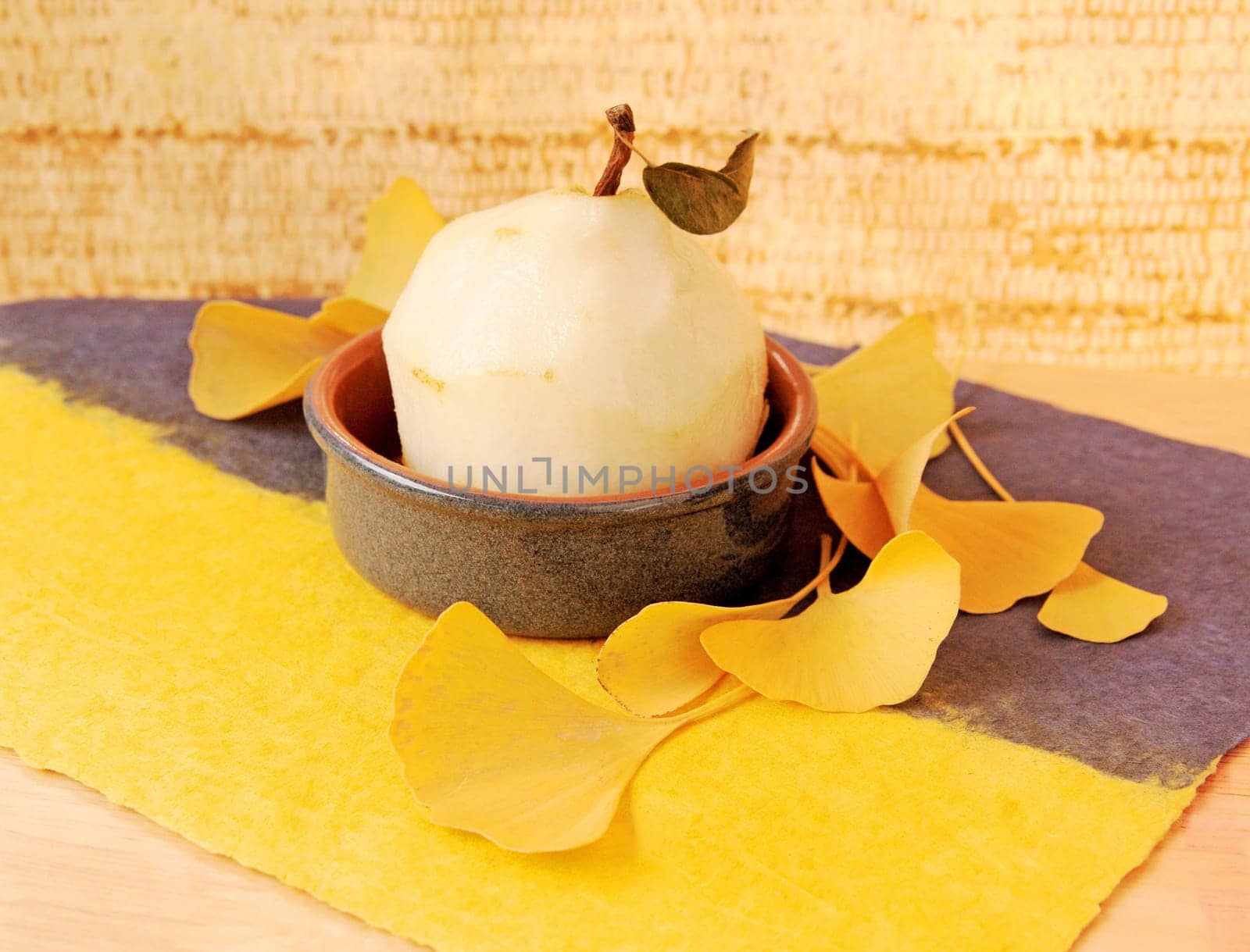 Peeled fruit in a small dish with autumn yellow ginkgo leaves on textured paper with copy space