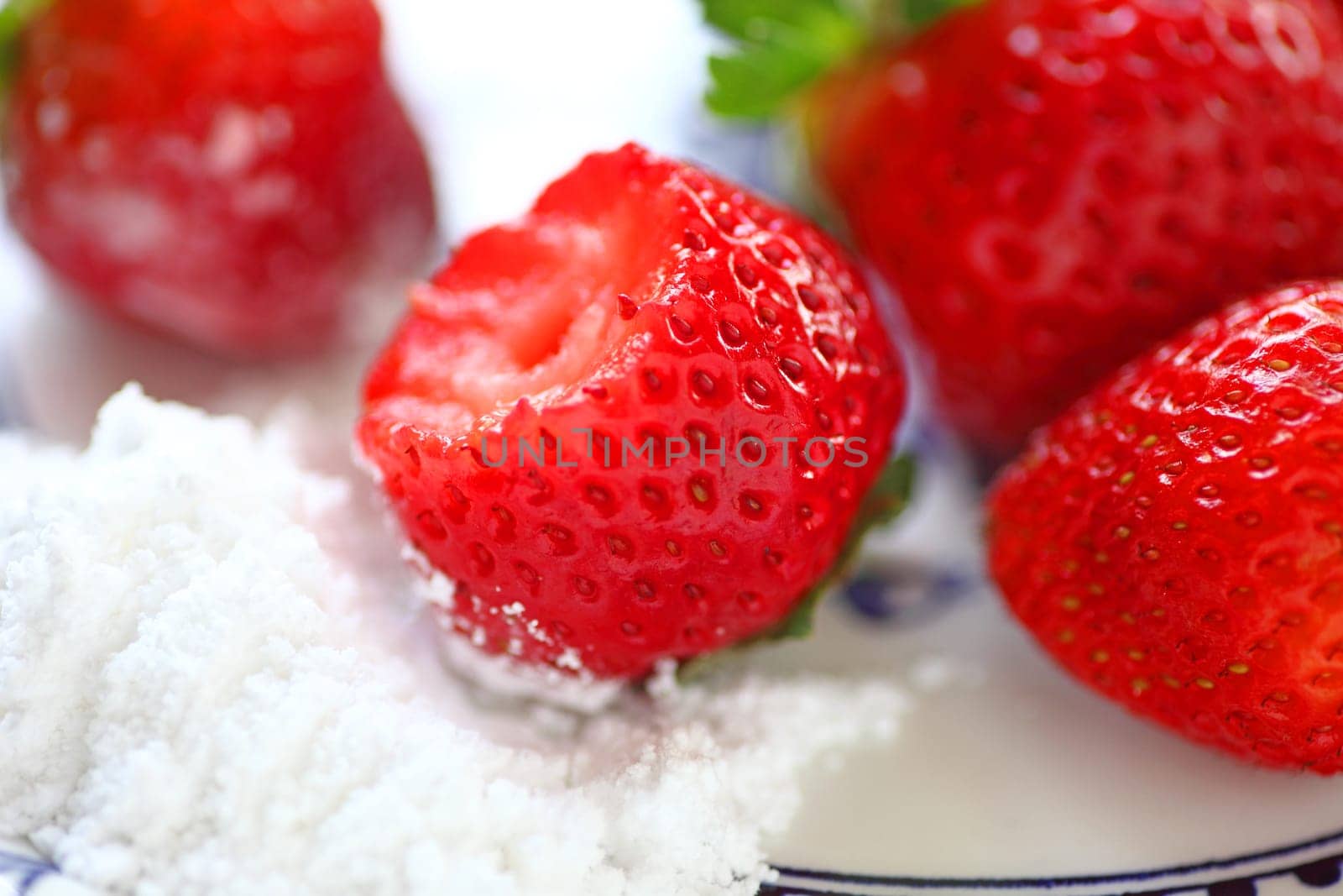 Fresh strawberries to dip in pile of powdered sugar, bite taken