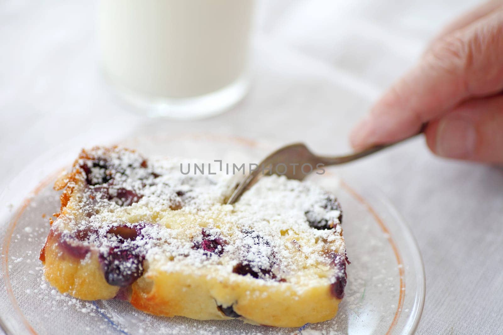 A man cutting into a slice of blueberry cake dusted with powdered sugar