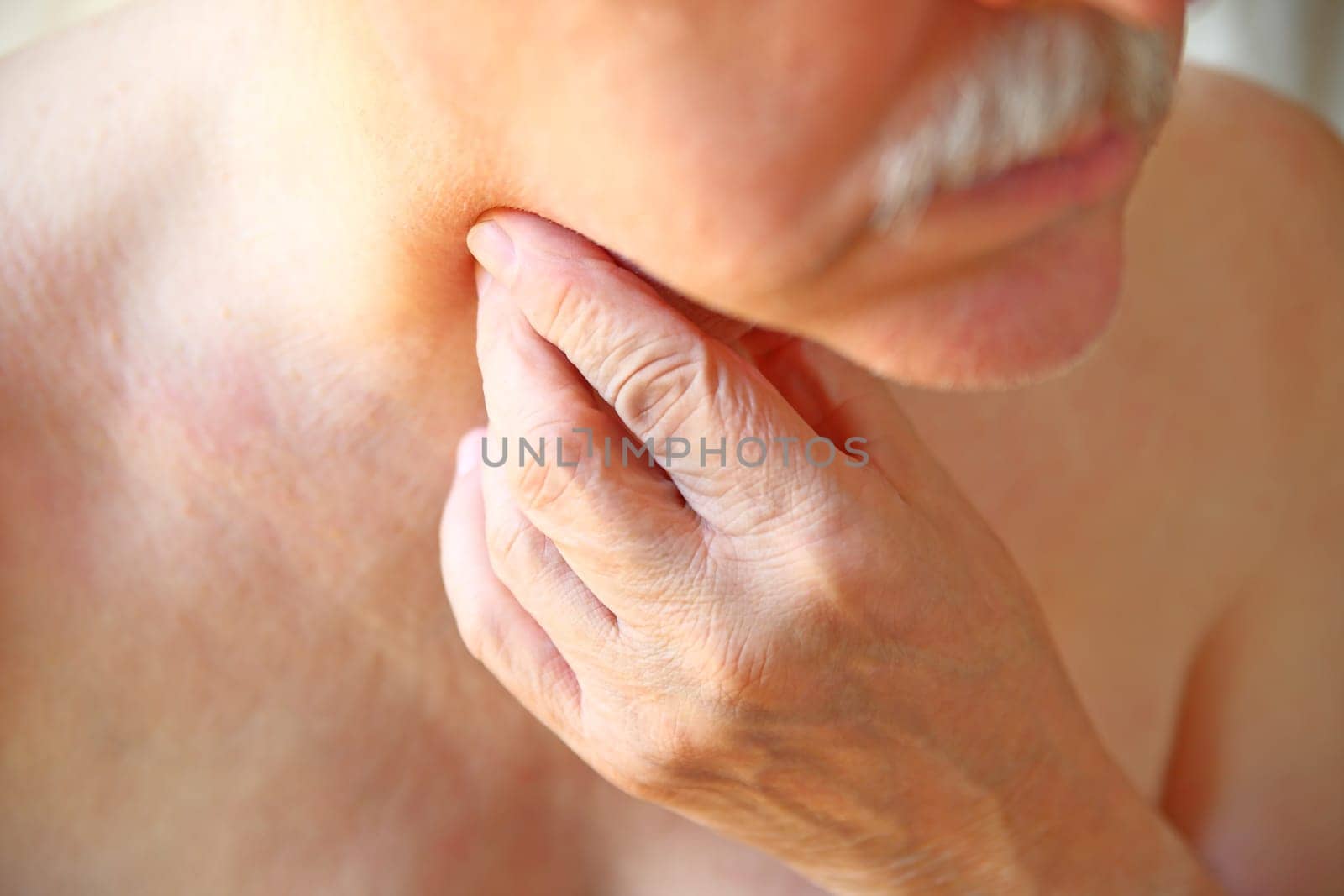 An older man touches his painful throat with his fingers