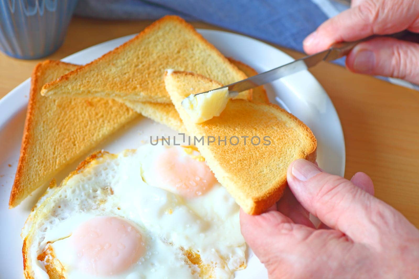Fried eggs and toast on a platter with man buttering toast triangle