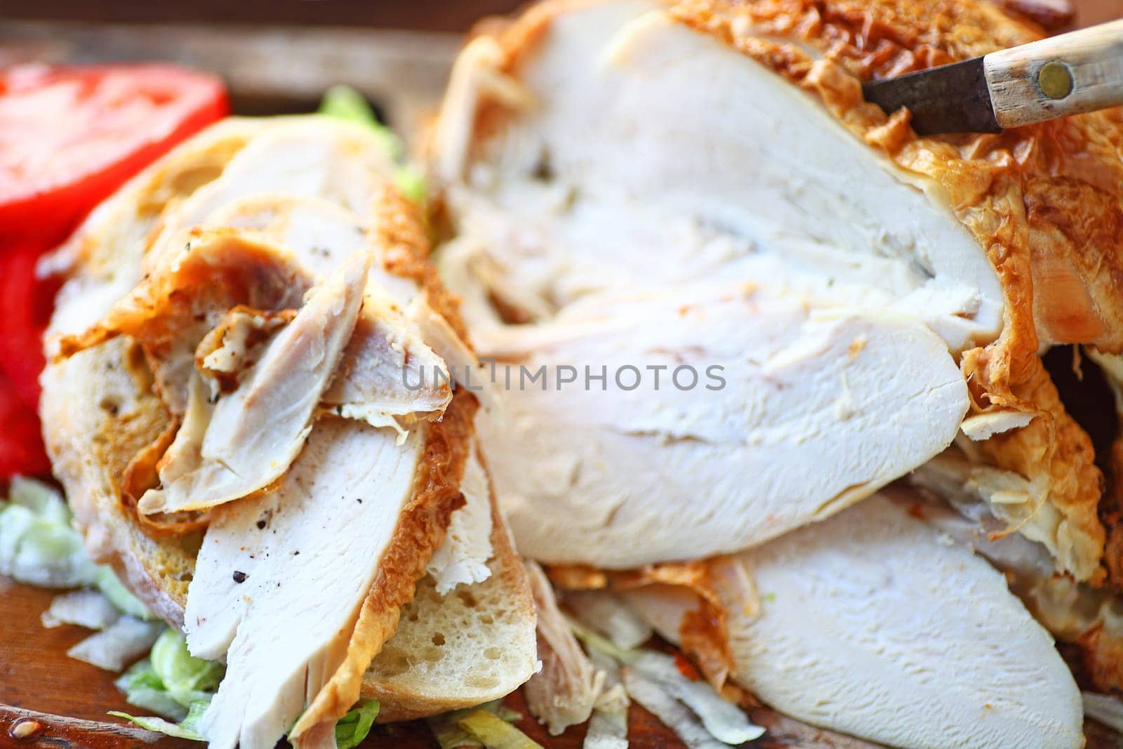 Sandwich made from a store-bought roast chicken with tomato slices and knife