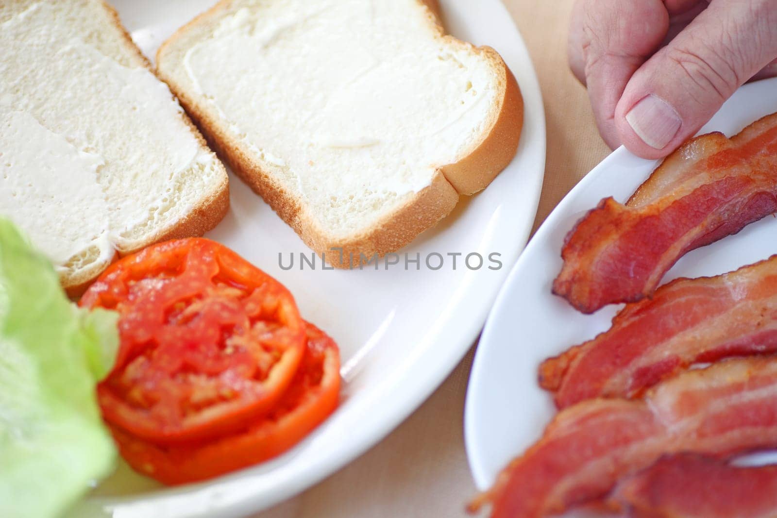 A man gets ready to put together a bacon, lettuce and tomato sandwich on white bread.