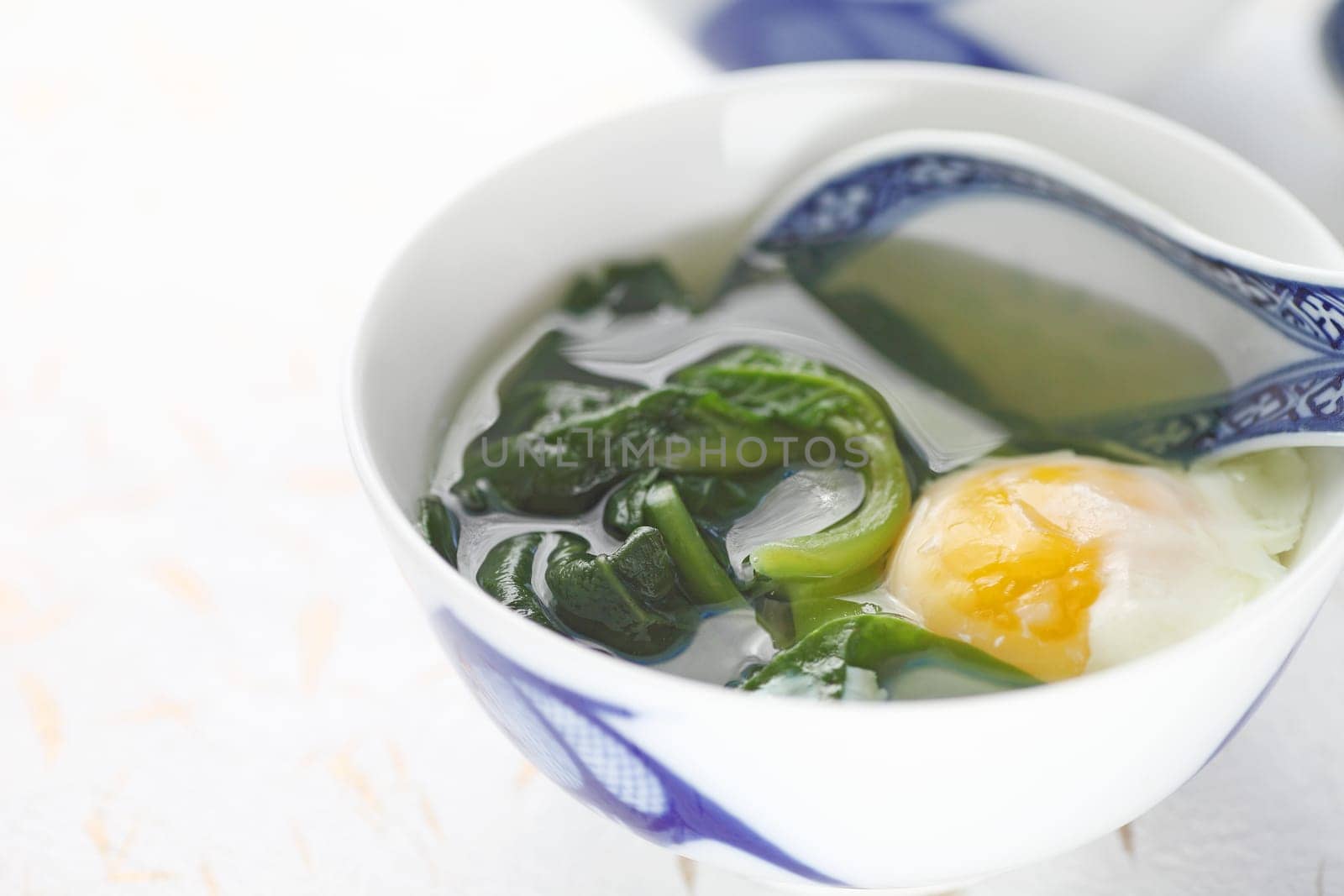 Malabar spinach soup with poached egg in Chinese bowl with spoon and copy space
