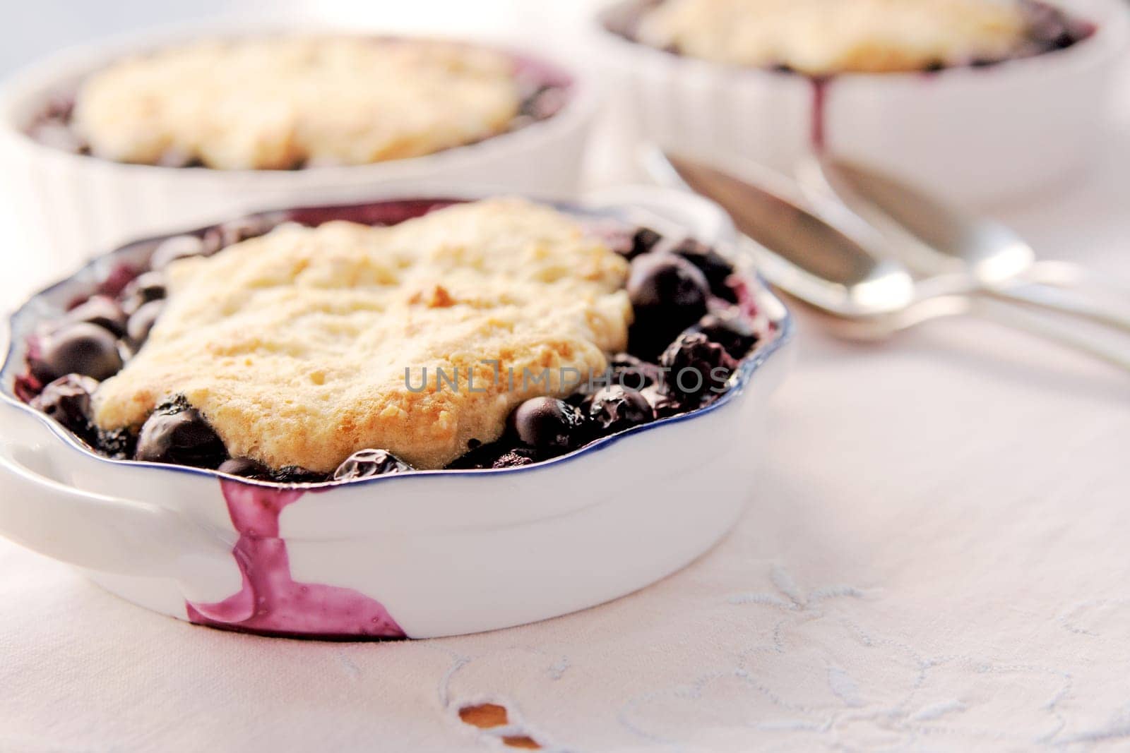 blueberry cobblers, desserts, blueberries, fresh fruit, homemade food, home cooking, white napkin, closeup, spoons, copy space, room for text, sweet, baked, natural light, textures, studio shot, indoors, no people.