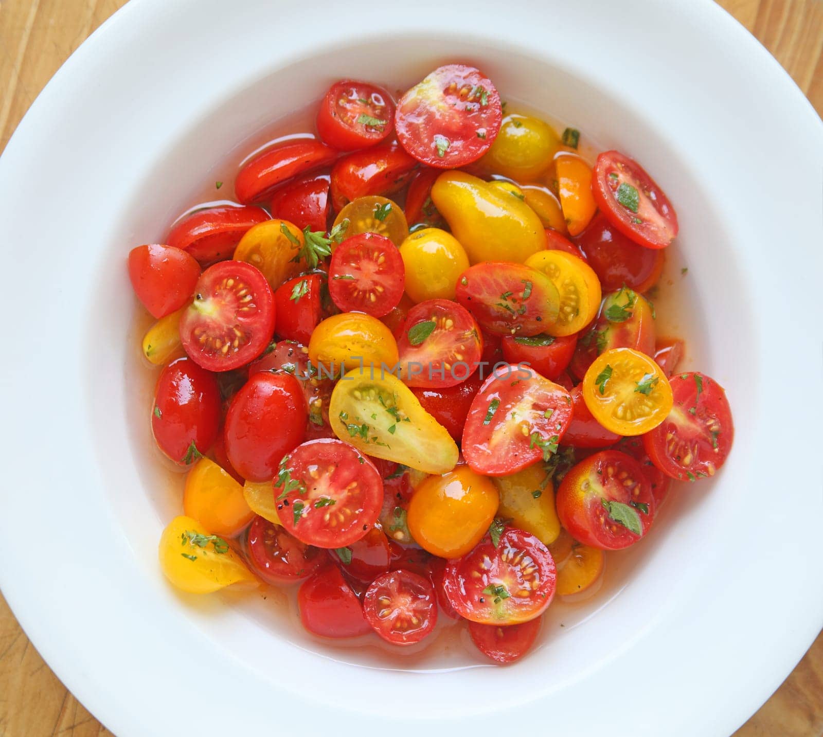 Assorted varieties and shapes of ripe cherry tomatoes marinating in a white dish from overhead