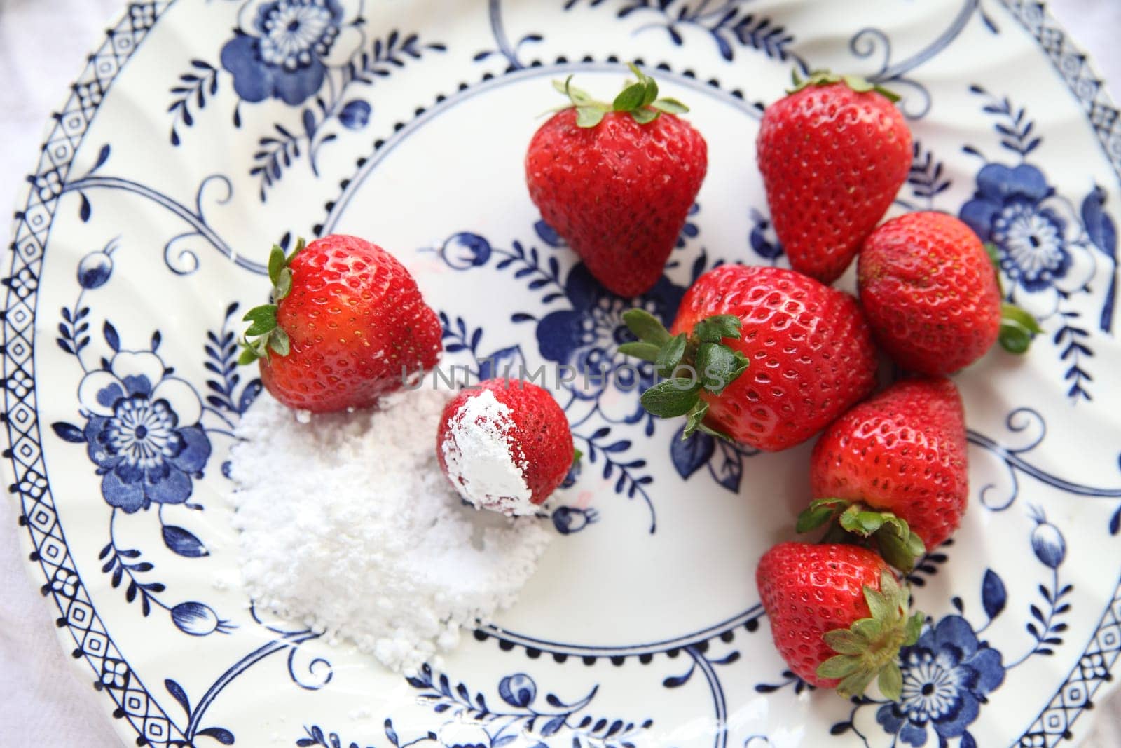 Overhead view of a decorative plate with fresh strawberries and powdered sugar