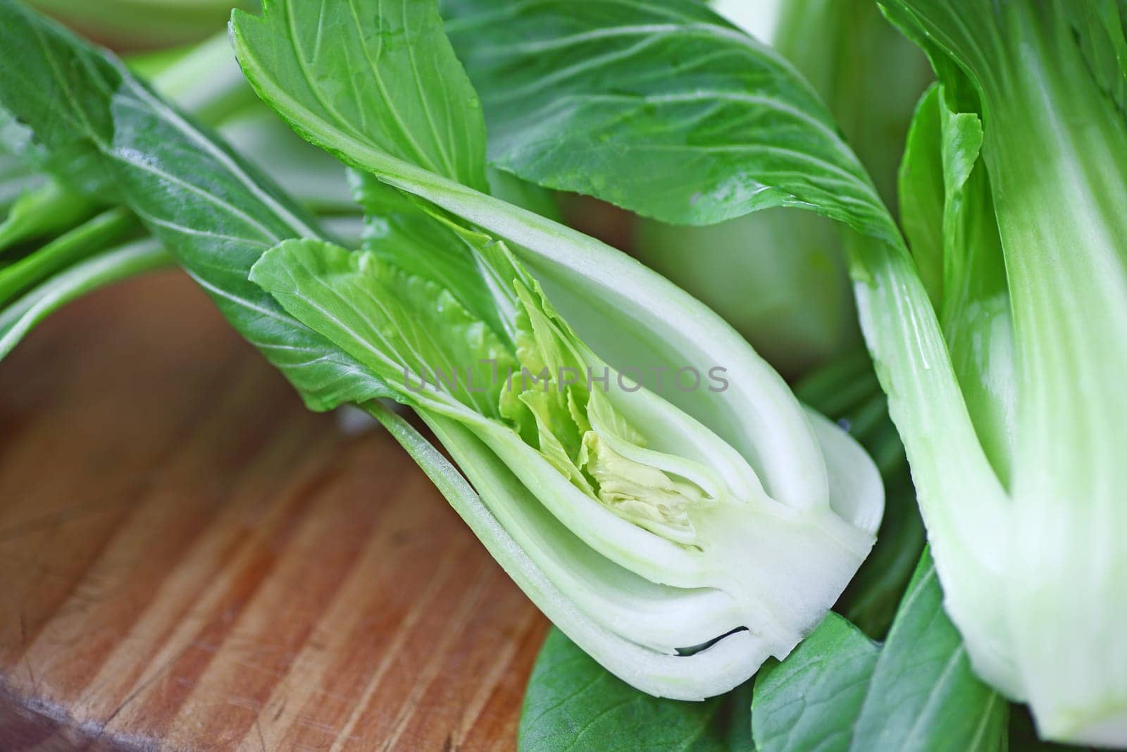 Fresh baby bok choy, one cut in half on cutting board with copy space