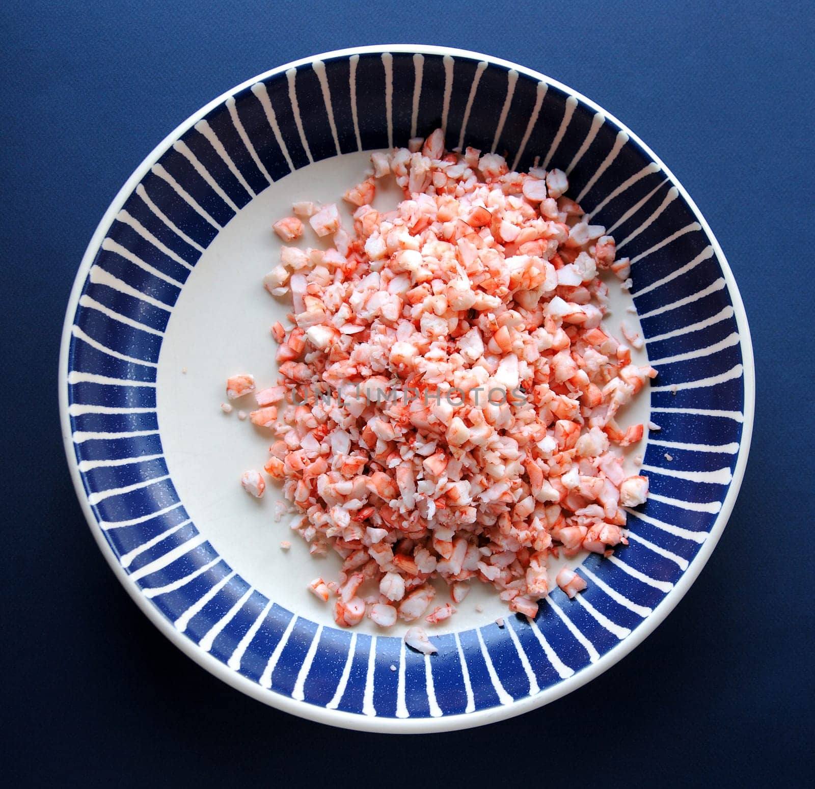 Cooked shrimp chopped in a dark blue and white bowl on a blue background