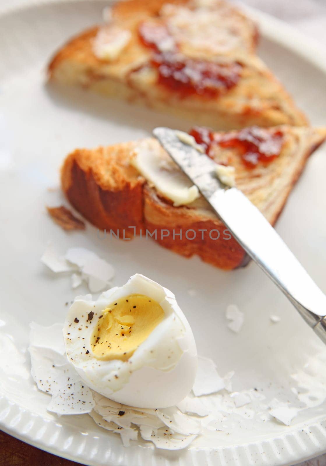 partially-peeled boiled egg with toast spread with butter and jam