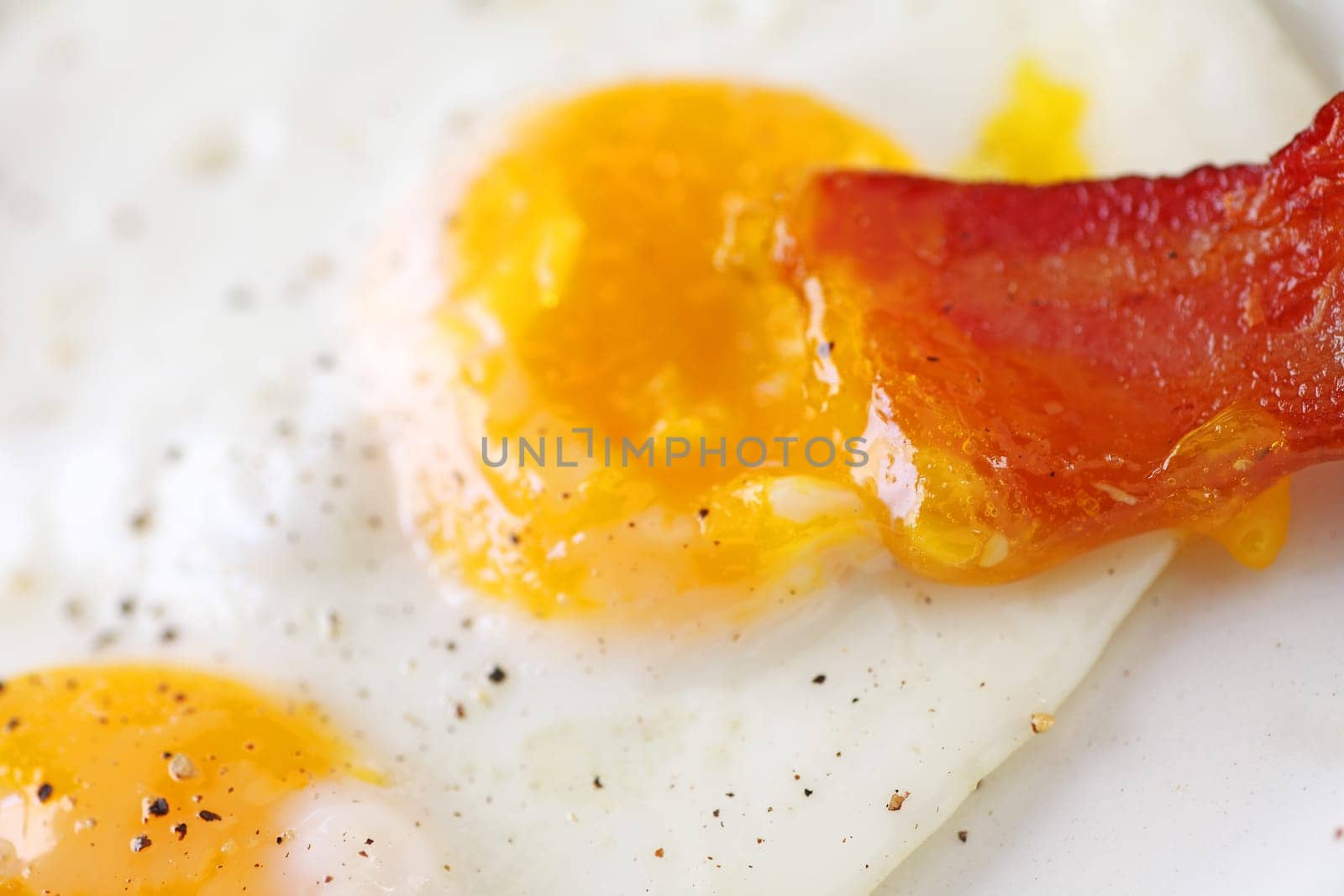 Extreme closeup of bacon slice dipped in runny egg yolk
