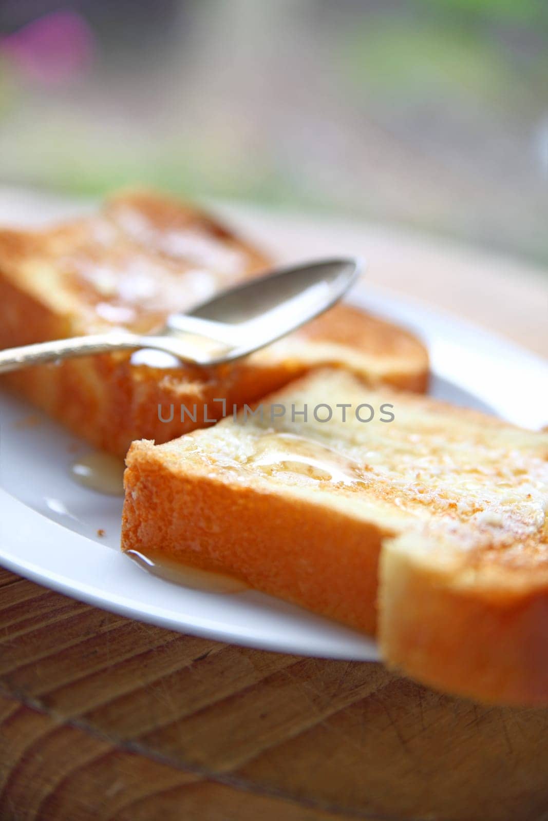 two slices of brioche toast spread wih butter and unfiltered honey with spoon