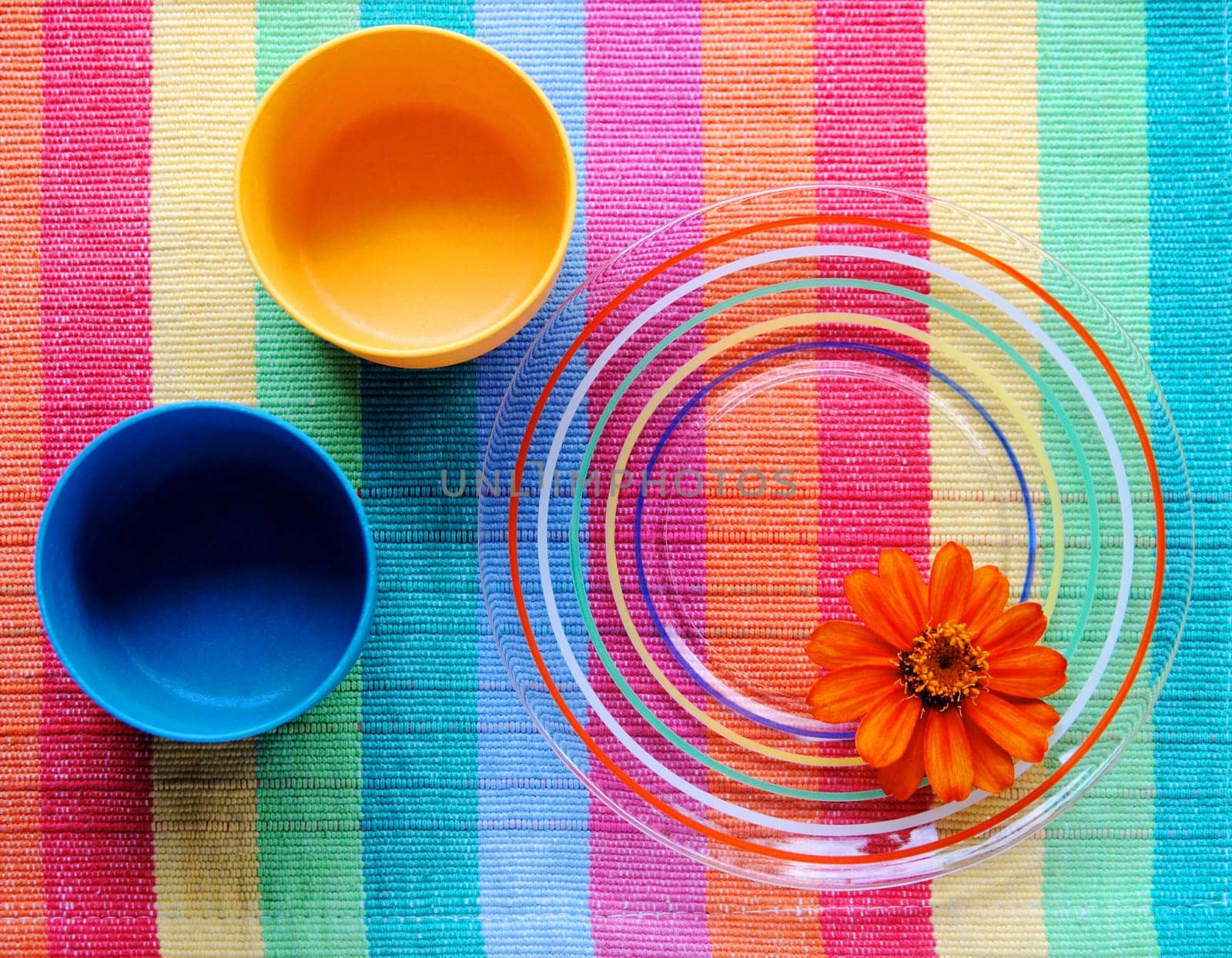 Glass dish with colorful design on a placemat with two plastic cups and a zinnia