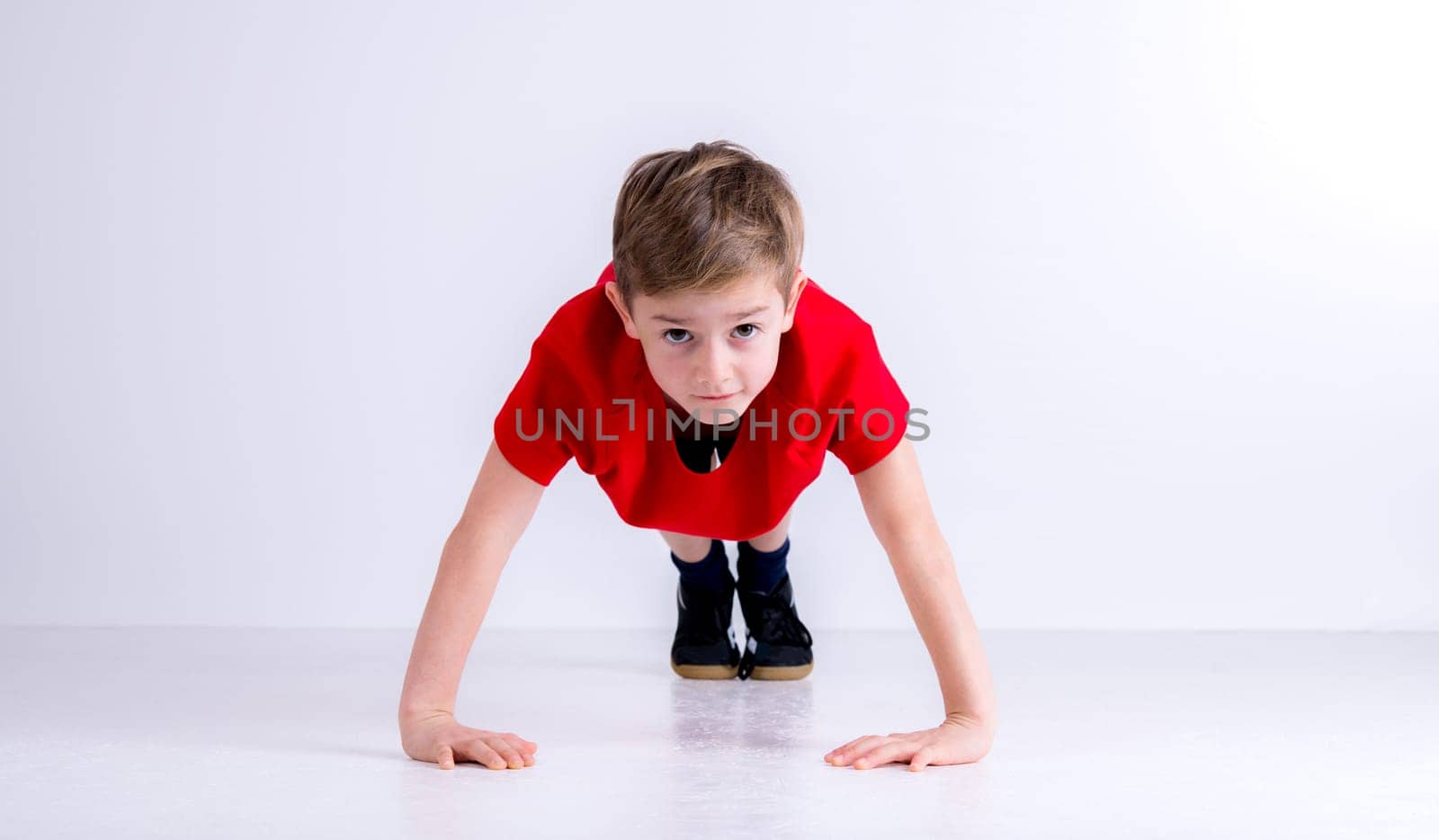 boy in red shirt doing push- ups in front of white background