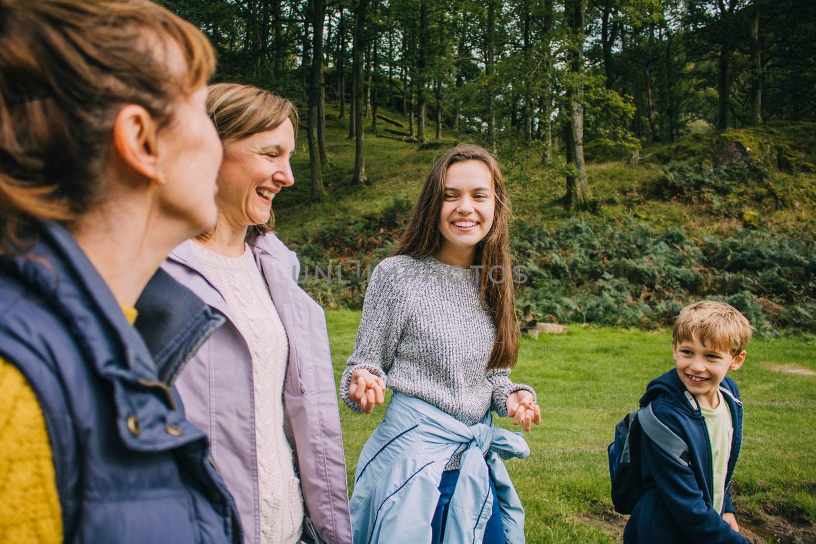 Teenage girl and her little borther are talking to their mother and grandmother as they hike through the woodlands together.