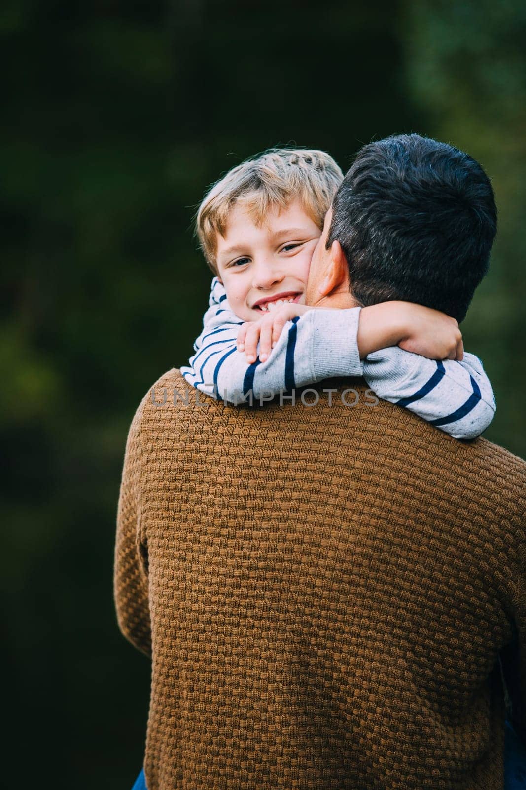Little boy is being cuddled tight by his father whilst outdoors.