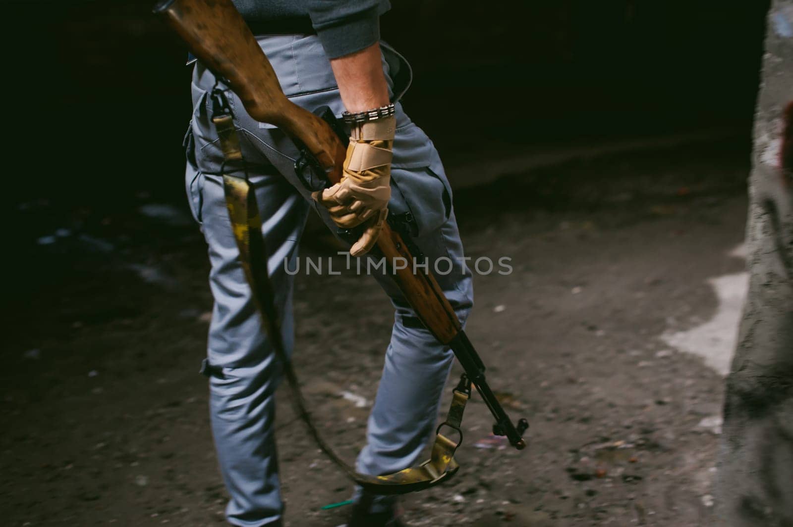 Athletic man in gray clothes with a carbine gun in his hand. Close-up of tactical gloves with weapons