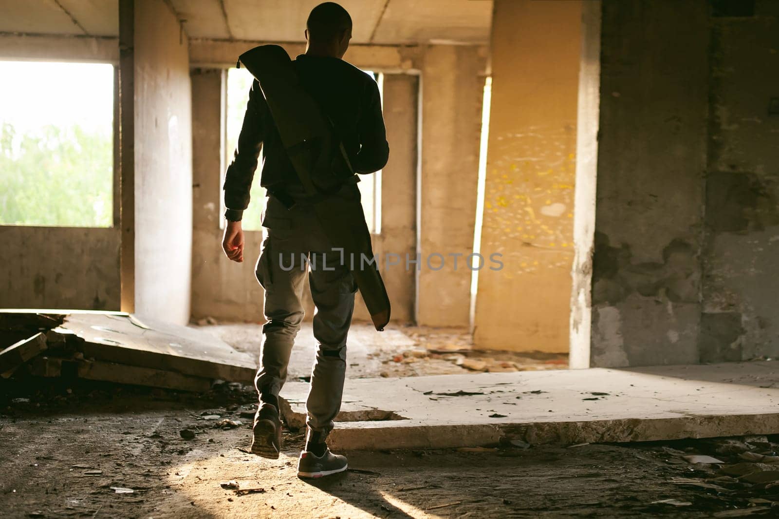 Athletic man walks through the ruins, with a cover for a gun for weeping, warm rays of light in the window
