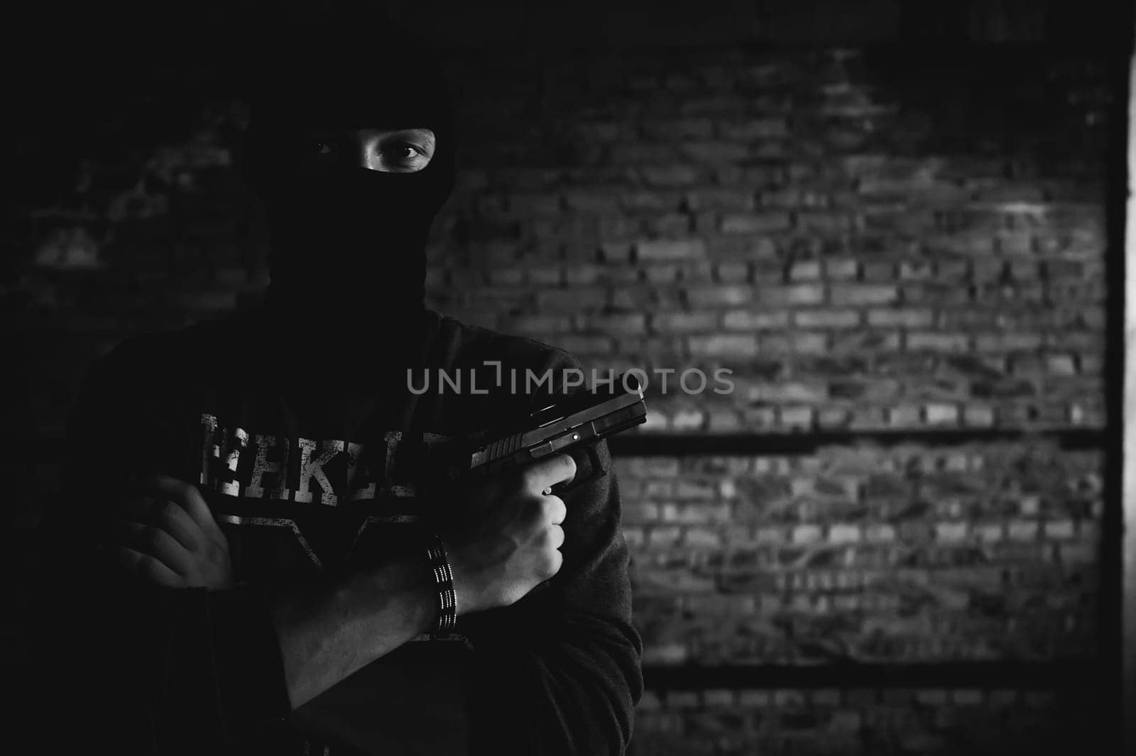 Athletic man in a balaclava, ski mask on his head, holds a gun in his hand, with his arms crossed over his chest