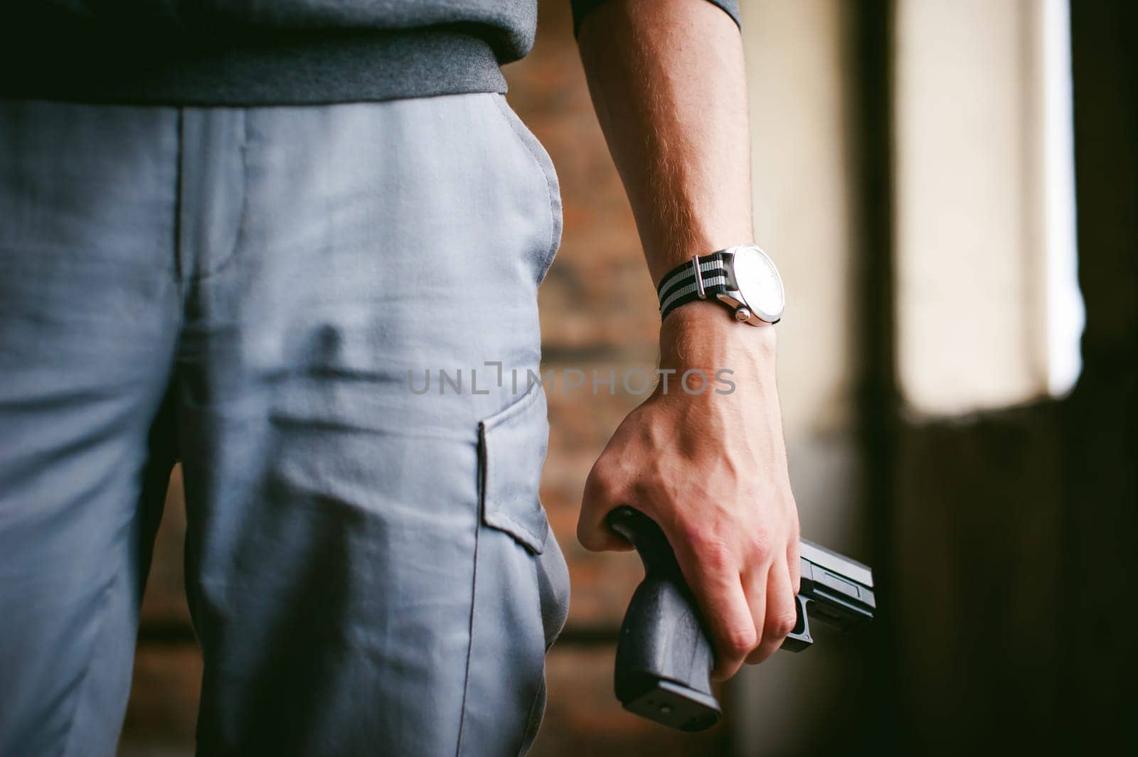 Dangerous athletic man, holds a gun in his hands, close-up. Wristband and watch