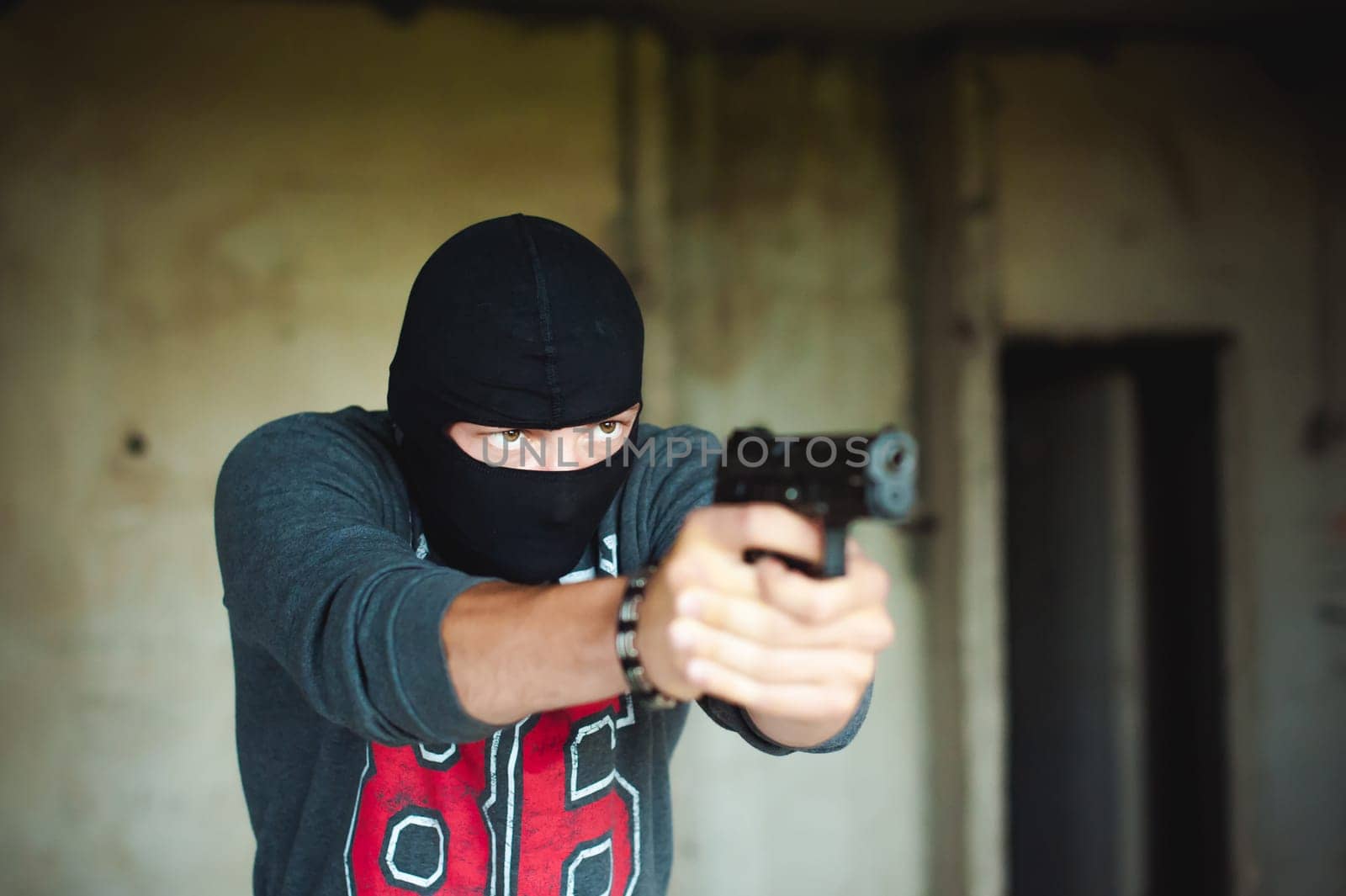 Athletic man in a balaclava, holds a pistol in his hand, is threatened with shooting, aiming