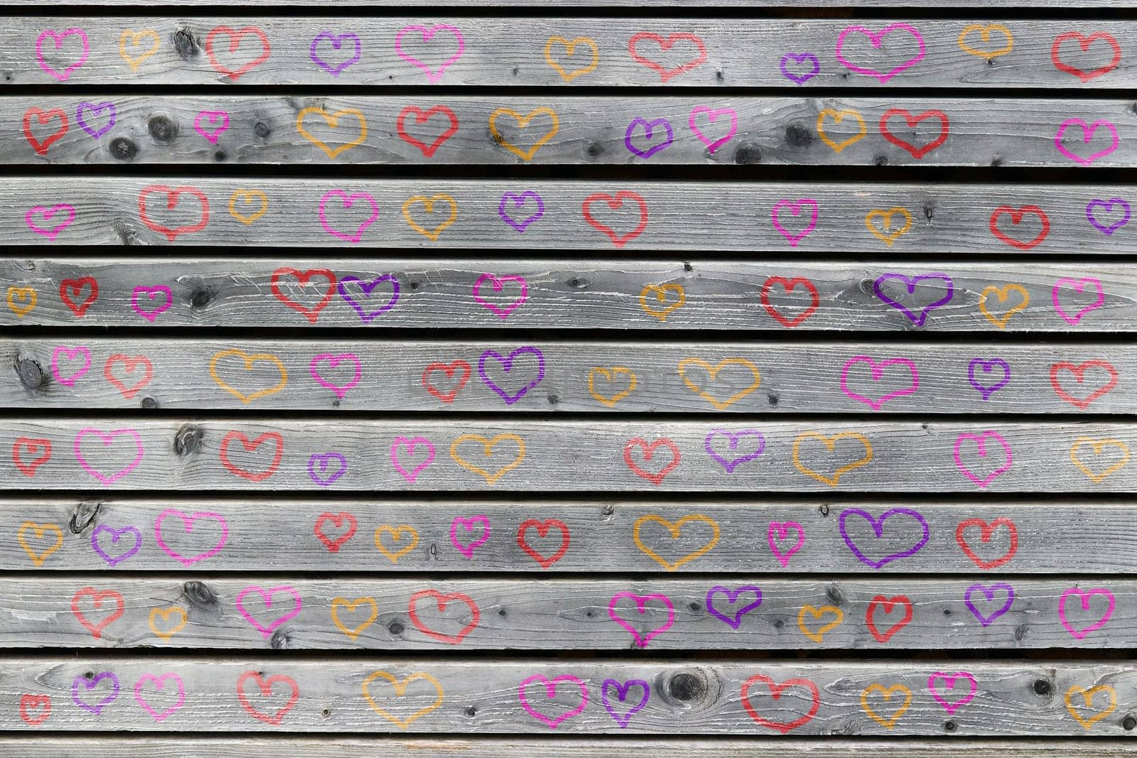 A wall of gray wood with many colorful hearts. Painted hearts on a gray wooden wall