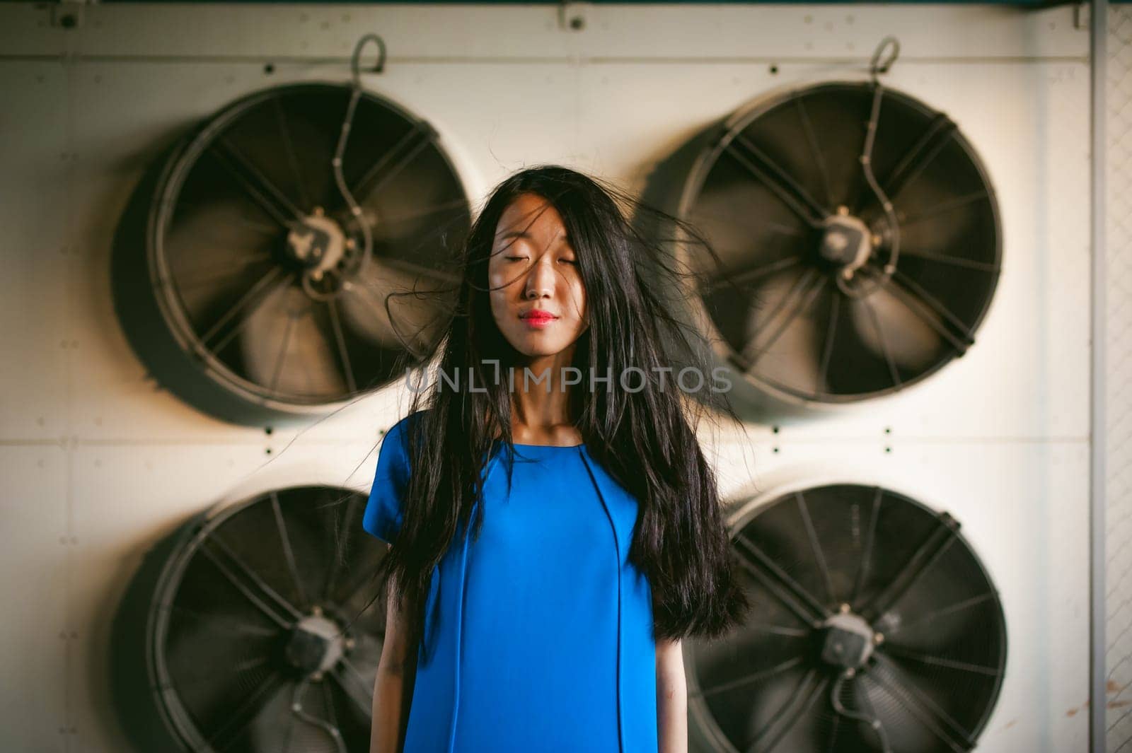 Young beautiful asian woman, on the background of industrial air conditioning system fans. Portrait of a girl with flying hair