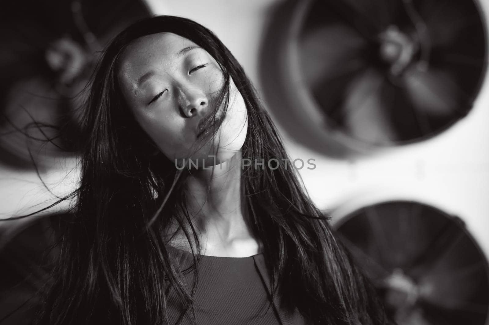Young beautiful asian woman, on the background of industrial air conditioning system fans. Portrait of a girl with flying hair