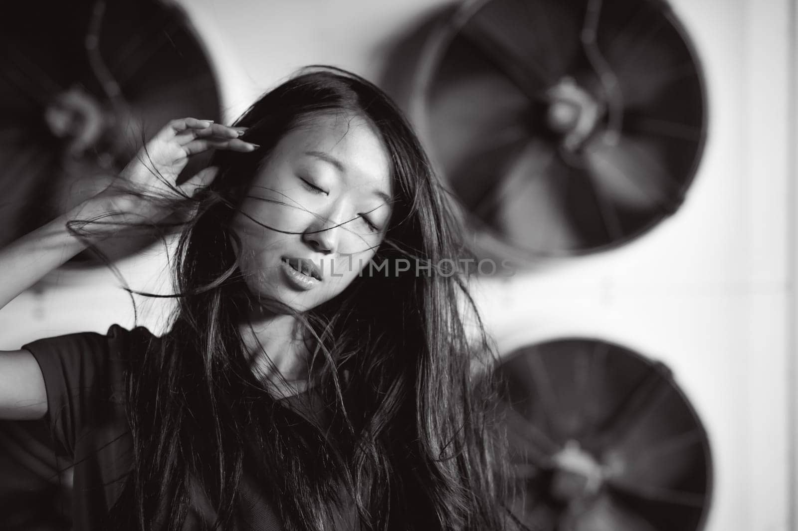Young beautiful asian woman, on the background of industrial air conditioning system fans. Portrait of a girl with flying hair