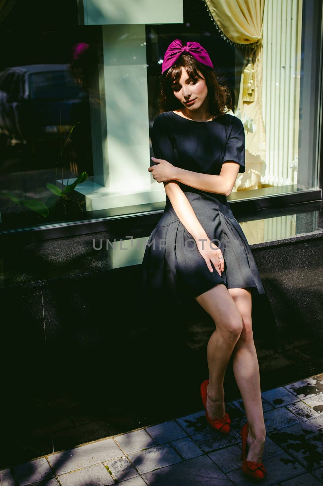 Beautiful woman in a dark stylish dress strolls along the street, near boutiques. Slender legs in red shoes