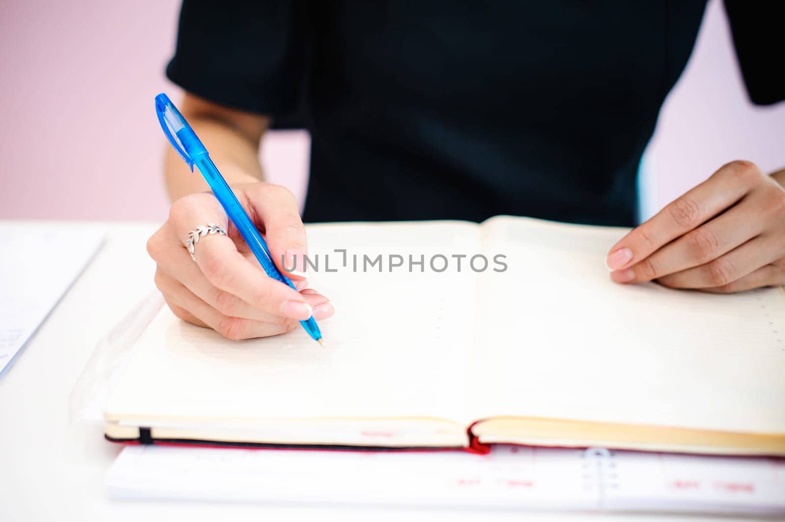 Business woman making notes in notepad. Beautiful well-groomed hands close-up hands, holding a pen, sitting in the workplace