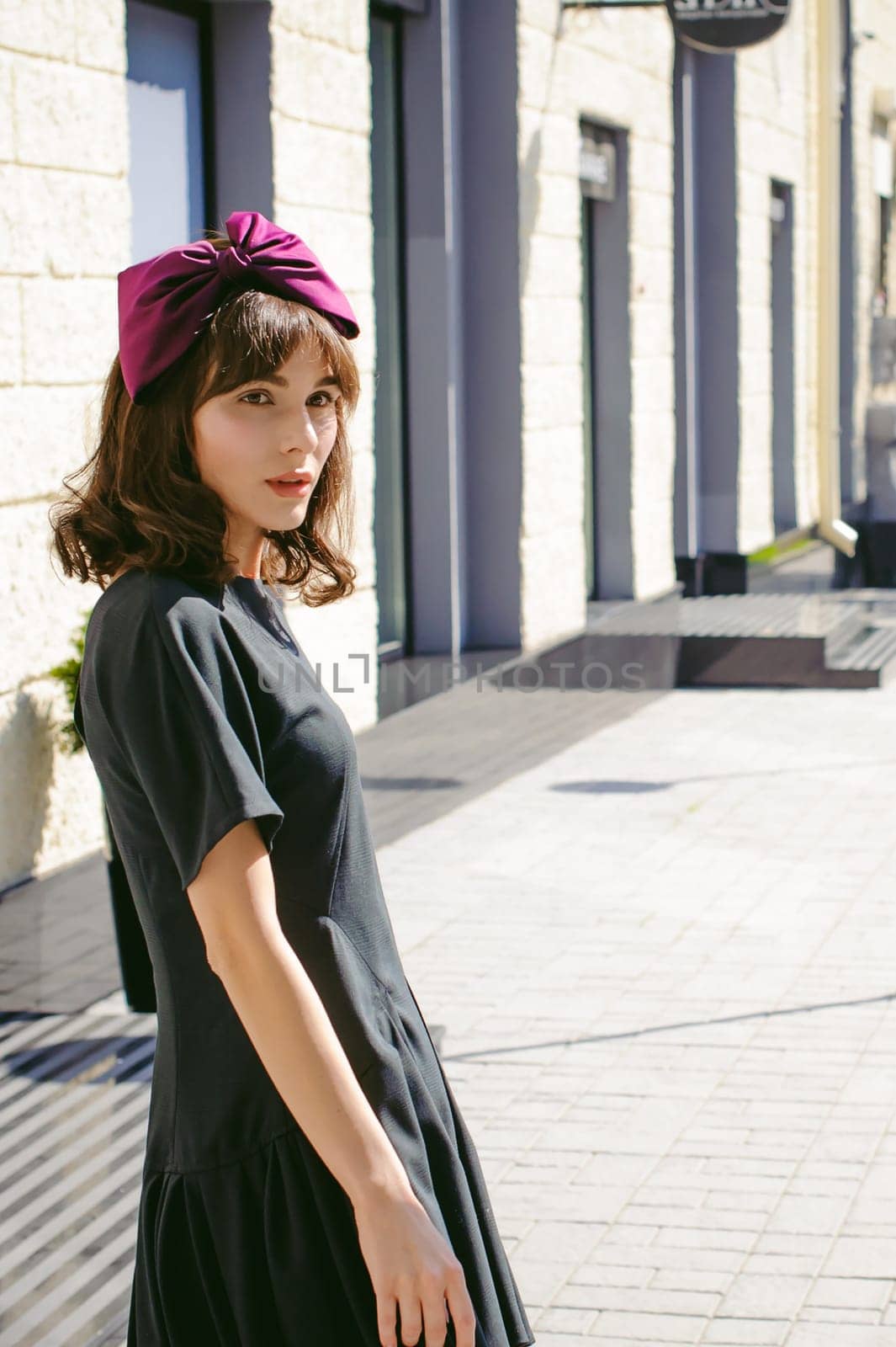 Beautiful woman in a dark stylish dress strolls along the street, near boutiques. Portrait of a fashionable girl