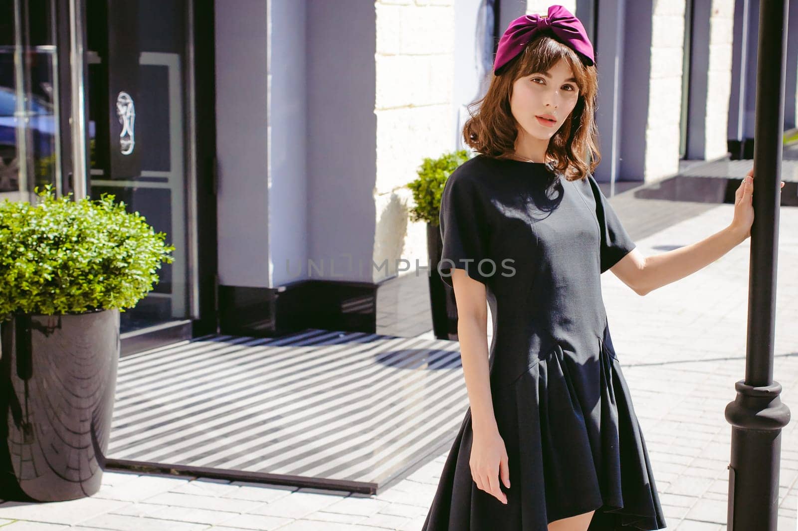 Beautiful woman in a dark stylish dress strolls along the street, near boutiques. Portrait of a fashionable girl