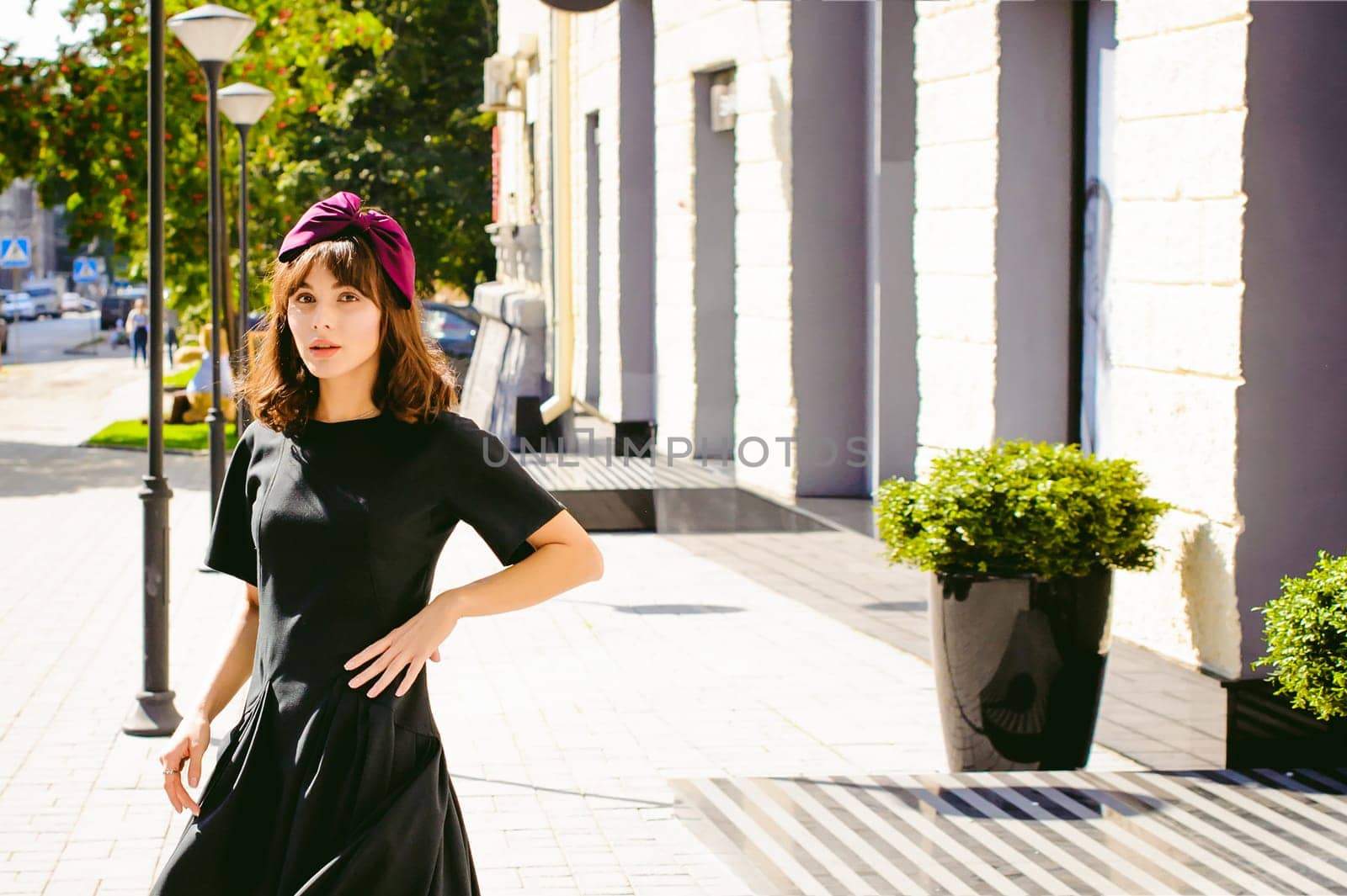 Beautiful woman in a dark stylish dress strolls along the street, near boutiques. Portrait of a fashionable girl