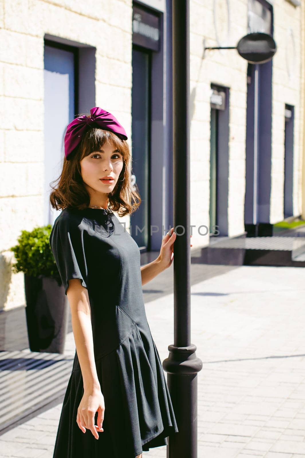 Beautiful woman in a dark stylish dress strolls along the street, near boutiques. Portrait of a fashionable girl